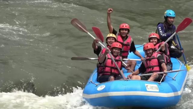 Gambar sekelompok pemuda sedang menikmati rafting di sebuah sungai.