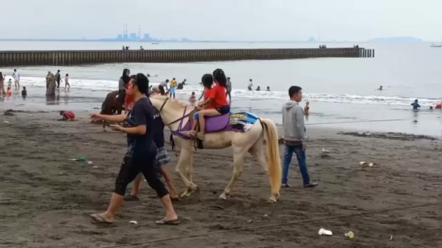 Gambar dua orang anak menunggangi kuda putih di bibir pantai.