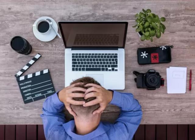 Gambar seseorang yang nampak memegang kepalanya di depan sebuah laptop.