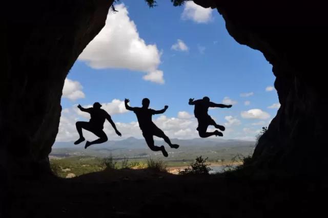 Gambar bayangan tiga orang yang sedang melompat di sebuah gua.