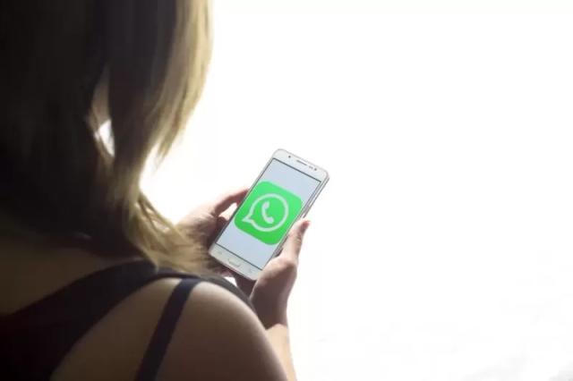 Gambar seorang wanita sedang memegang smartphone berisi logo WhatsApp bewarna hijau.