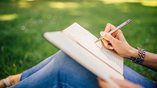 Gambar tangan seorang wanita yang sedang menuliskan sesuatu di buku catatan.