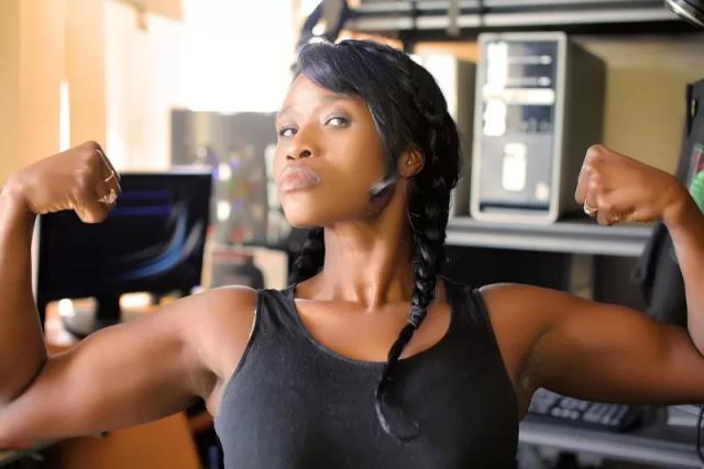 Seorang wanita berbaju hitam sedang berpose menunjukkan otot lengannya, ilustrasi kata-kata motivasi kuat diet bagi pemula.