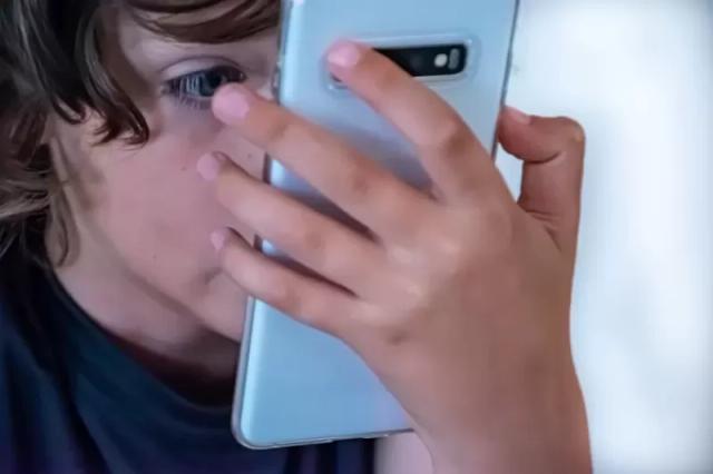 Potret seorang anak kecil sedang memegang sebuah smartphone tepat di depan matanya.