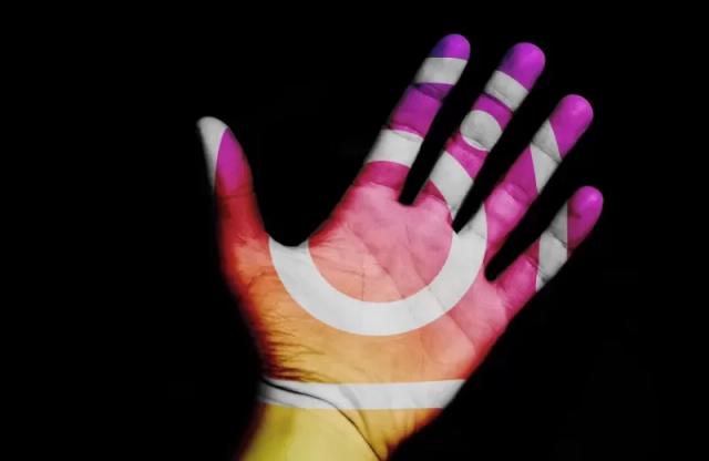 Gambar sebuah tangan dengan bayangan logo Instagram berwarna pelangi.