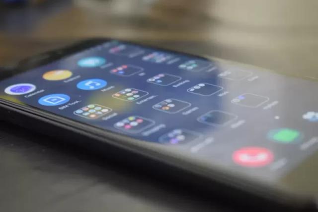 Gambar sebuah smartphone berwarna hitam dalam kondisi hidup di atas meja, ilustrasi cara mengamankan kontak WA dari pinjaman online.