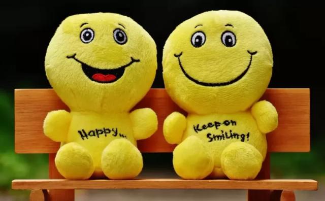 Gambar dua buah boneka emoji bewarna kuning duduk di atas kursi.