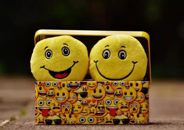 Gambar dua buah boneka emoji berwarna kuning di atas kotak.