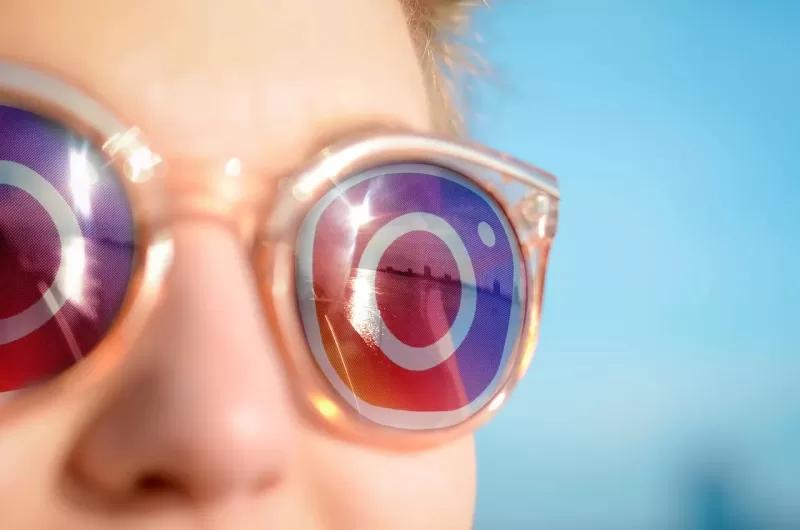 Gambar orang dengan kacamata yang berisi pantulan logo Instagram, ilustrasi cara membedakan profil asli dan palsu di IG