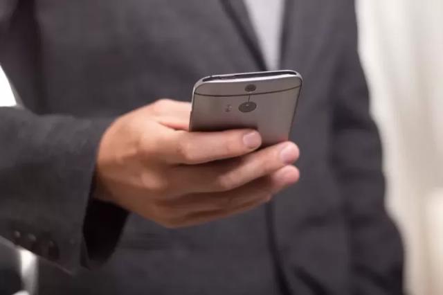 Potret seorang pria berjas hitam sedang memegang smartphone
