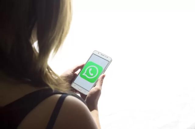 Gambar seorang wanita sedang mlihat ponselnya yang berisi logo aplikasi WhatsApp bewarna hijau.