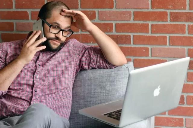 Gambar seseorang yang sedang menelepon dan menatap layar laptop, ilustrasi cara menghilangkan rasa capek yang berlebihan saat kerja.