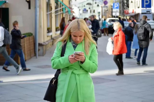 Gambar seorang wanita berbaju hijau sedang menggunakan ponselnya.