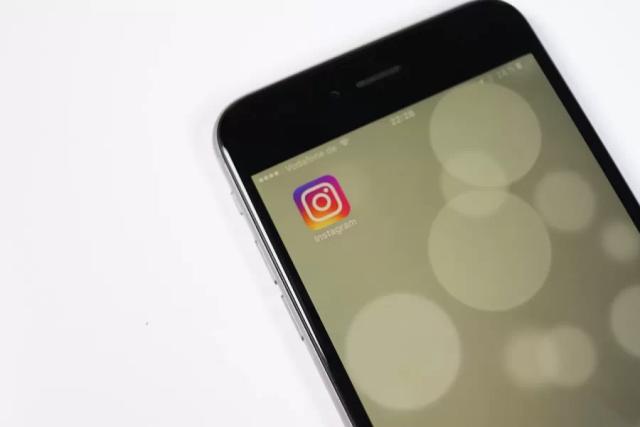 Gambar sebuah smartphone berwarna hitam yang menampilkan ikon Instagram, ilustrasi centang biru di Instagram.