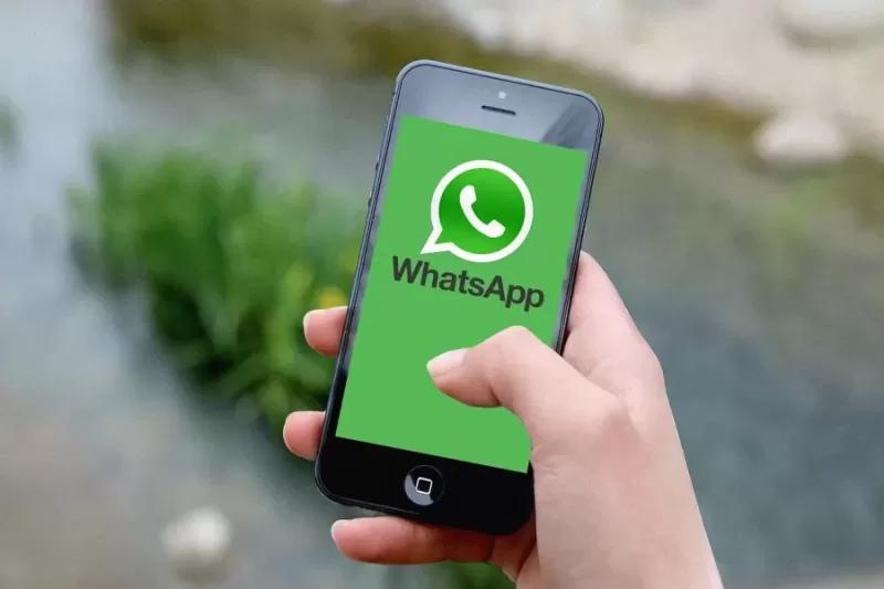 Gambar sebuah smartphone berisi logo aplikasi WhatsApp berwarna hijau yang sedang dipegang oleh seseorang, ilustrasi cara mengetahui penipu di WA.