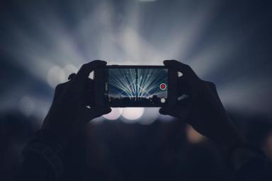 Gambar seseorang sedang memotret di sebuah konser menggunakan iPhone.