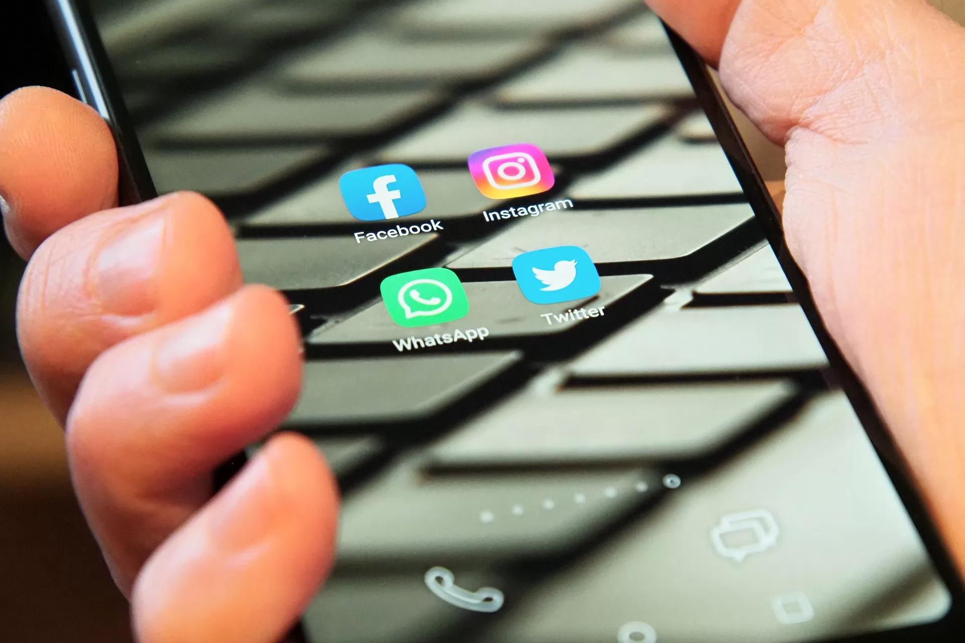 Gambar tangan seseorang sedang memegang sebuah smartphone yang berisi ikon-ikon media sosial, salah satunya WhatsApp, ilustrasi trik membuka WA tanpa ketahuan online.