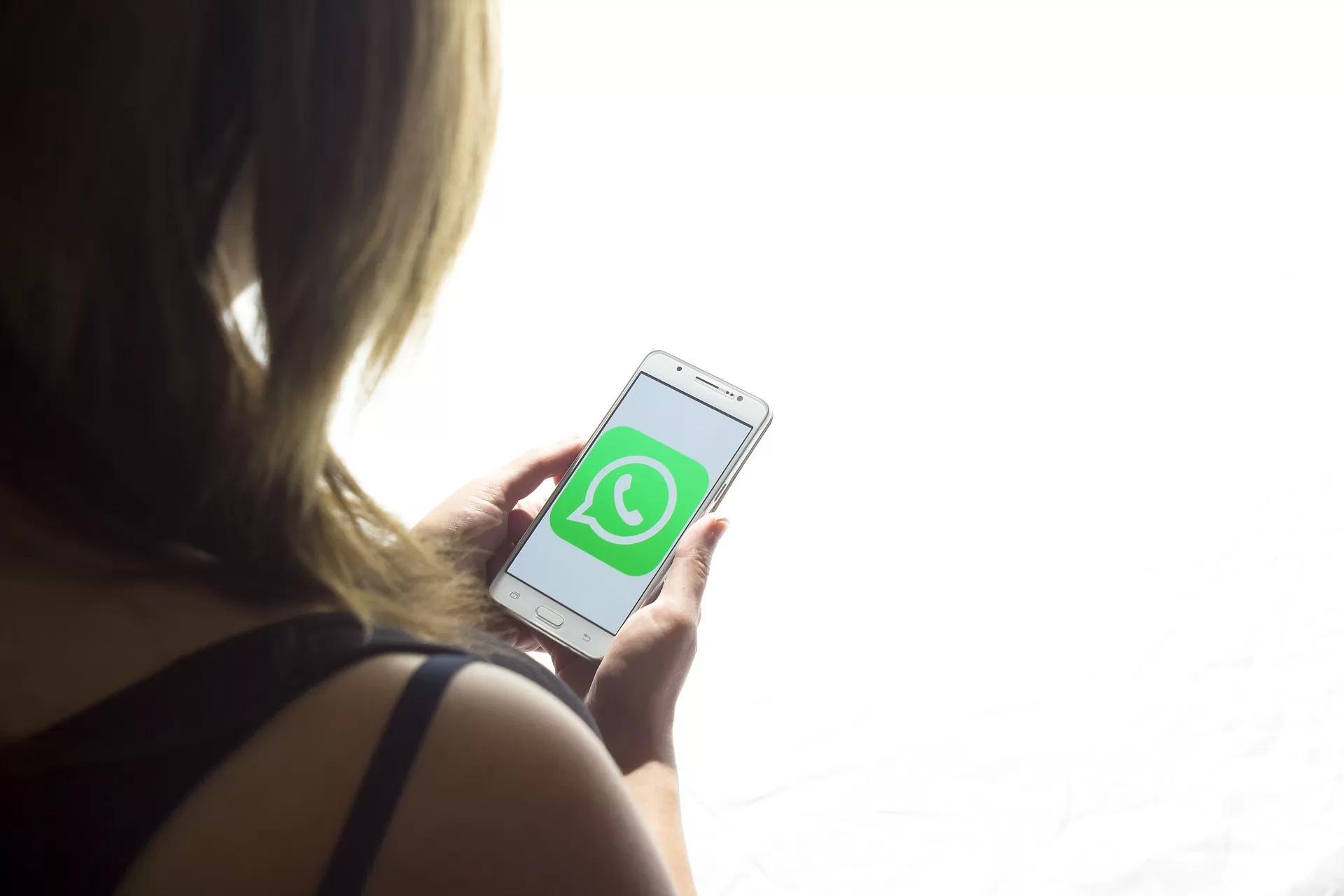 Seorang wanita yang sedang memegang smartphone berisi logo WhatsApp.