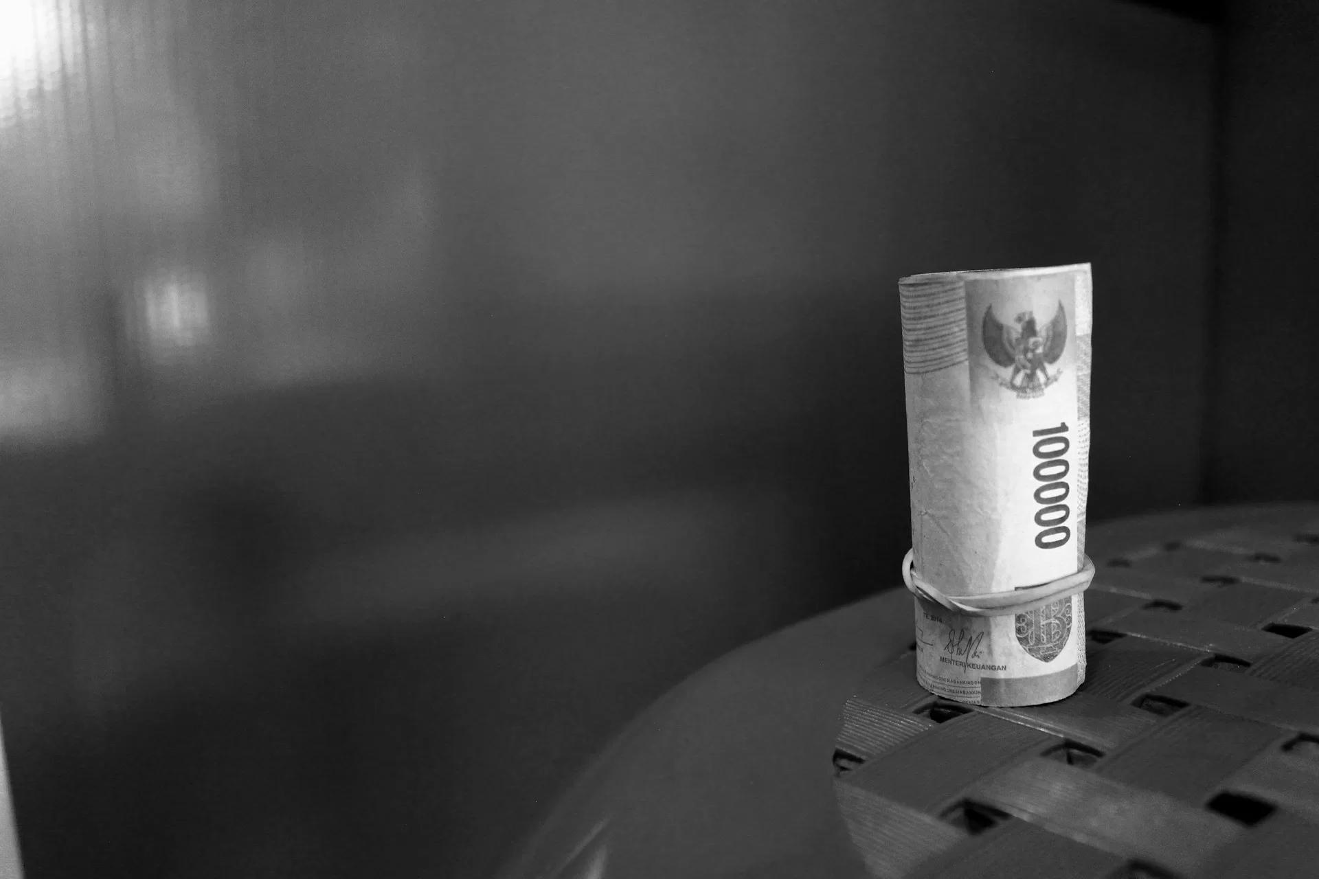 Gambar hitam putih uang ratusan ribu Rupiah yang digulung, ilustrasi cara mengatasi terlilit utang pinjol